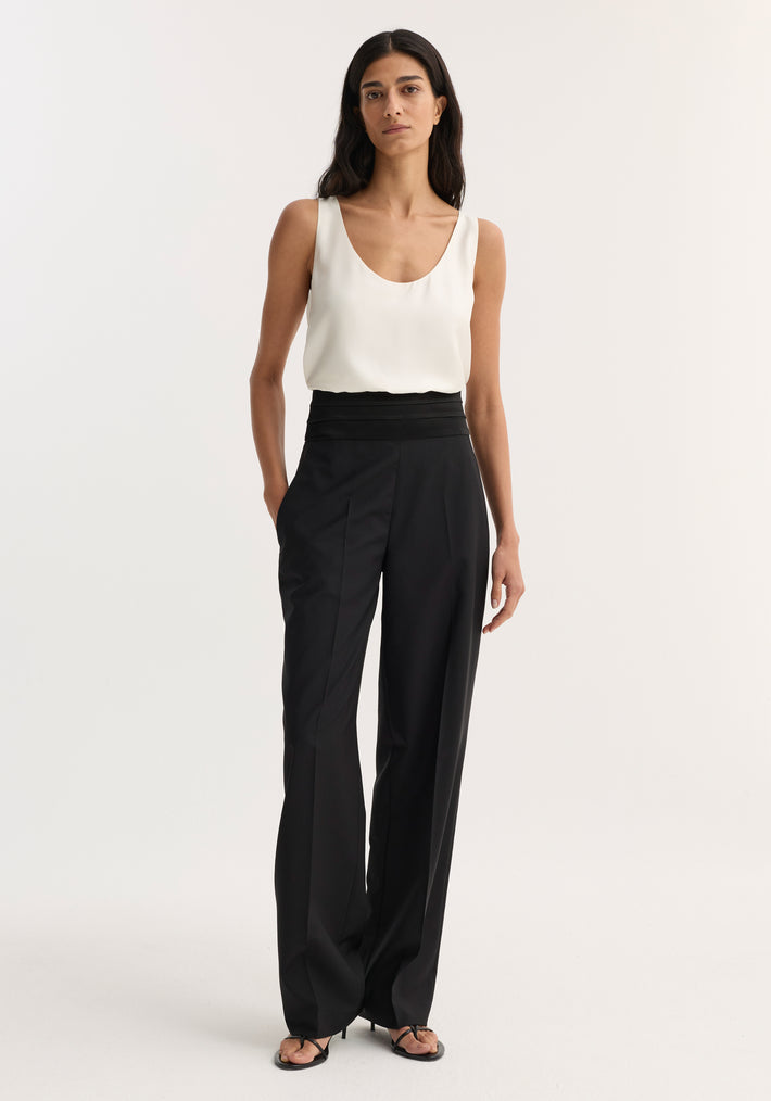 Woman wearing Satin Cumberband Trousers in black, showcasing a cummerbund waistband and slightly wide legs, paired with a sleeveless top and heeled sandals.