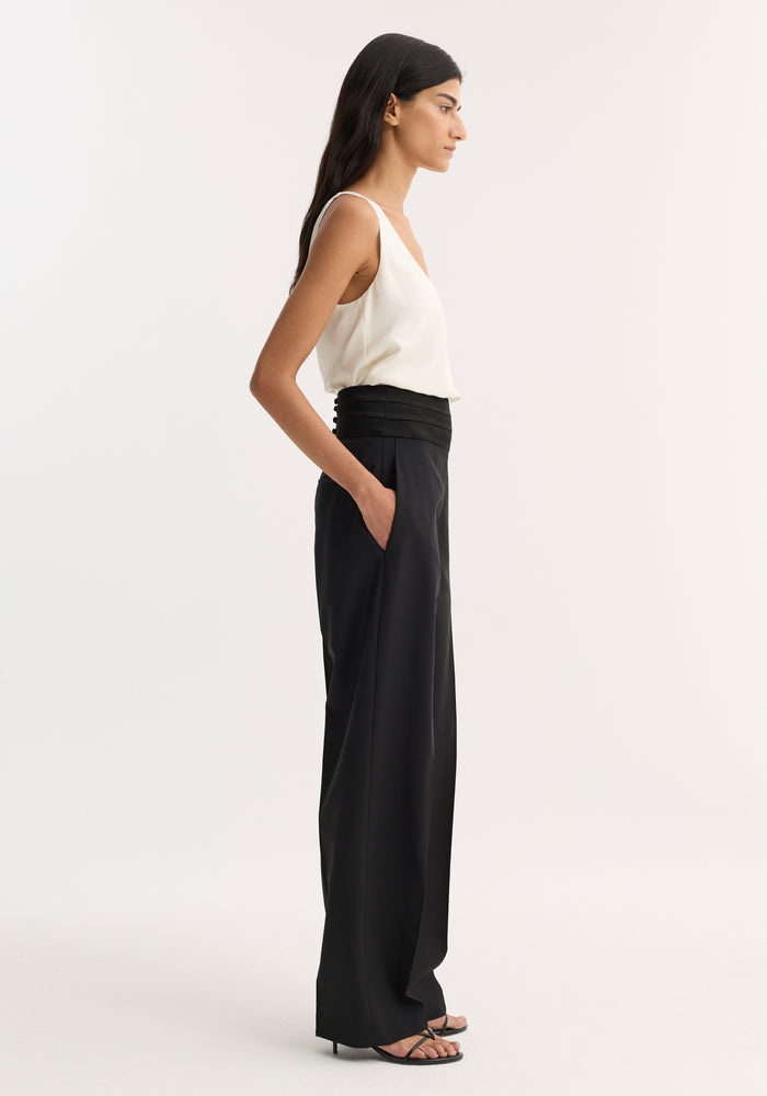 Model wearing Satin Cumberband Trousers in black, featuring a structured waistband and side pockets, paired with a cream V-neck camisole.