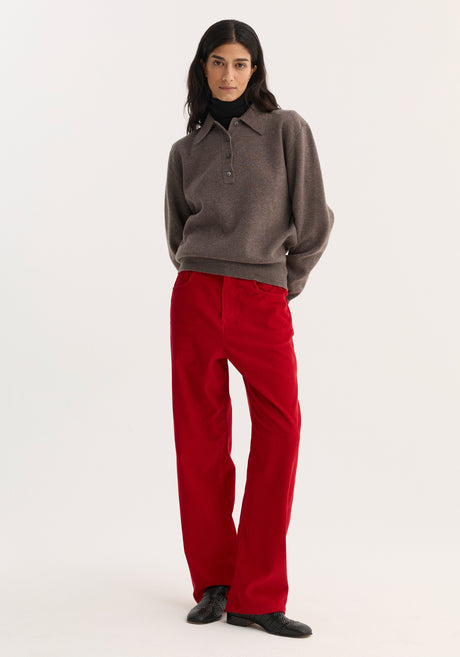 Woman wearing Relaxed Corduroy Trousers in Rosso, paired with a knit polo sweater and black shoes, showcasing the pants' vibrant hue and denim-inspired details.