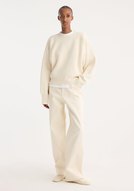 Person wearing Compact cotton trousers in off white, showcasing a wide-leg, baggy fit with low waist, styled with a chunky knit sweater and slip-on shoes.