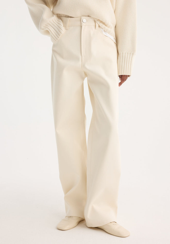 Person wearing Compact cotton trousers | off white, showcasing high-waisted, wide-leg design, paired with a tucked chunky knit sweater and pointed-toe loafers, one hand in pocket.