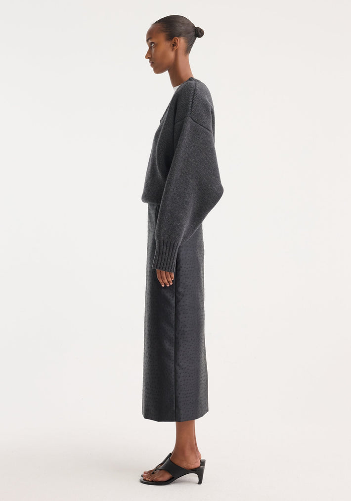 Model wearing Ostrich satin column skirt, showcasing its high-waisted, embossed ostrich-skin texture, paired with a charcoal-gray knit sweater and black heeled slides.