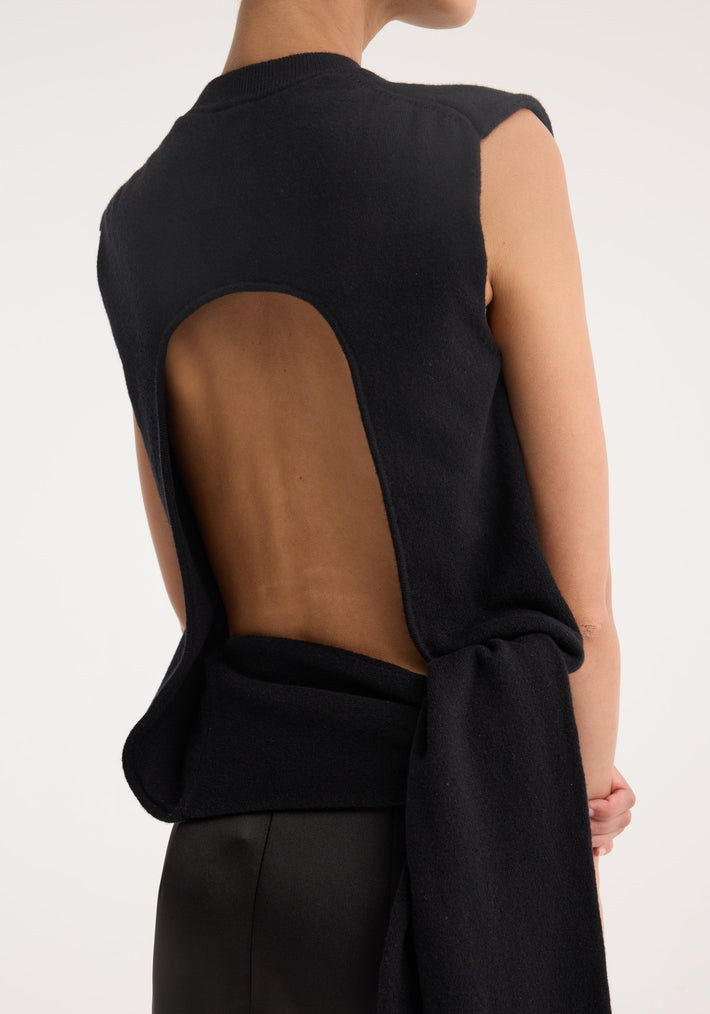 Person wearing an Open-back sash wrap top | black with U-shaped back cutout, tied at the waist, showcasing deconstructed sleeves and a fluid silhouette.