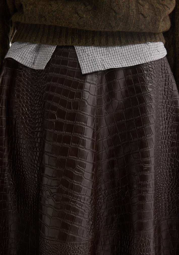 Close-up of A-line croco skirt in mahogany, showcasing its soft, embossed leather texture, layered over a small-check shirt and chunky knit sweater.