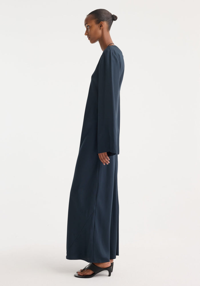 Model in a Signature silk dress | storm, featuring a minimalist, floor-length design with wide sleeves and a soft drape, paired with black sandals.