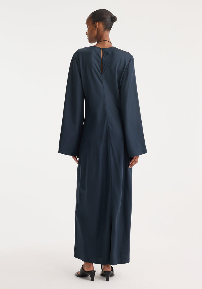 Back view of a woman in a Signature silk dress | storm, showcasing a minimalist, floor-length design with wide sleeves and a keyhole detail.