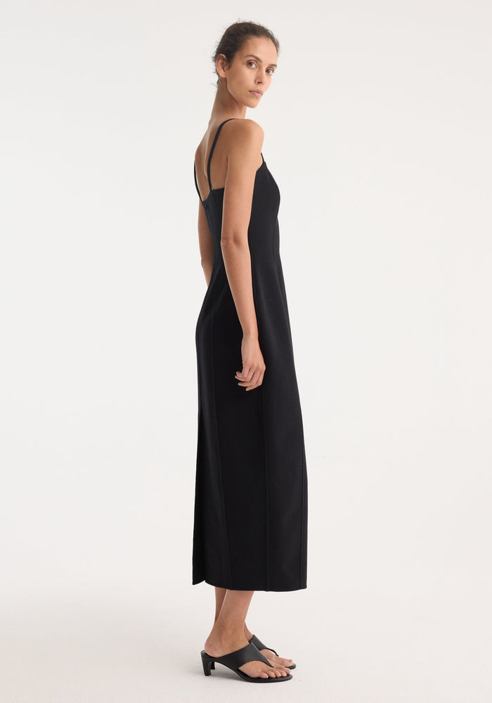 Woman modeling Sculptural double-faced dress | black, sleeveless with spaghetti straps, straight-cut silhouette, mid-calf length, subtle side slit, paired with low-heeled sandals.