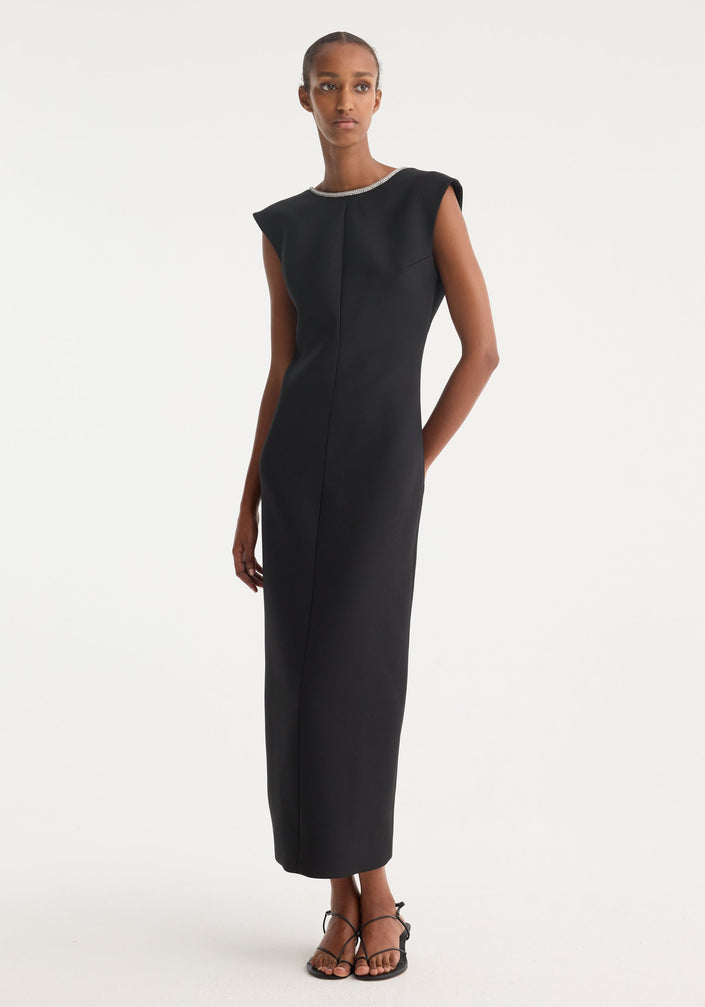 Open back appliqué dress | black: A woman in a form-fitting, sleeveless black maxi dress with a rhinestone neckline, open back, and caped shoulders, paired with black sandals.