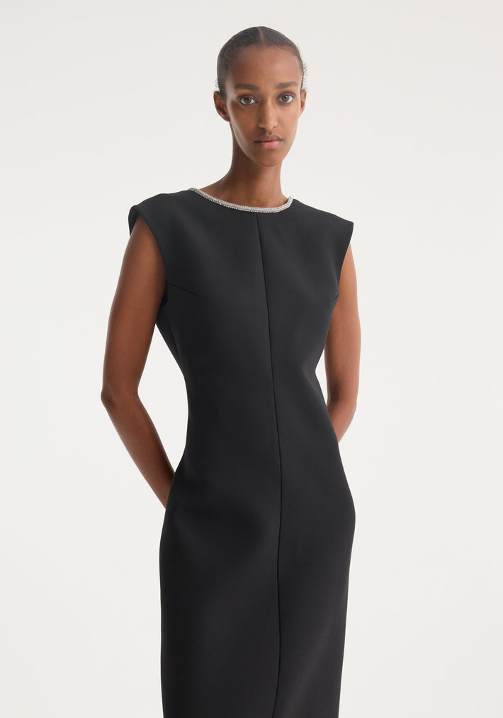 Model in an Open Back Appliqué Dress | Black, featuring a high neckline with crystal trim, showcasing form-fitting design against a light background.