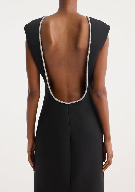 Open back appliqué dress | black: A woman in a form-fitting, sleeveless black maxi dress with a rhinestone neckline, open back, and caped shoulders, paired with black sandals.