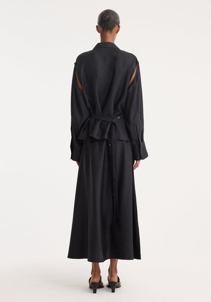 Silk gilet-dress in black, worn by model, features a deconstructed design with cut-out shoulders, self-tie belt, and button-down ankle-length skirt.