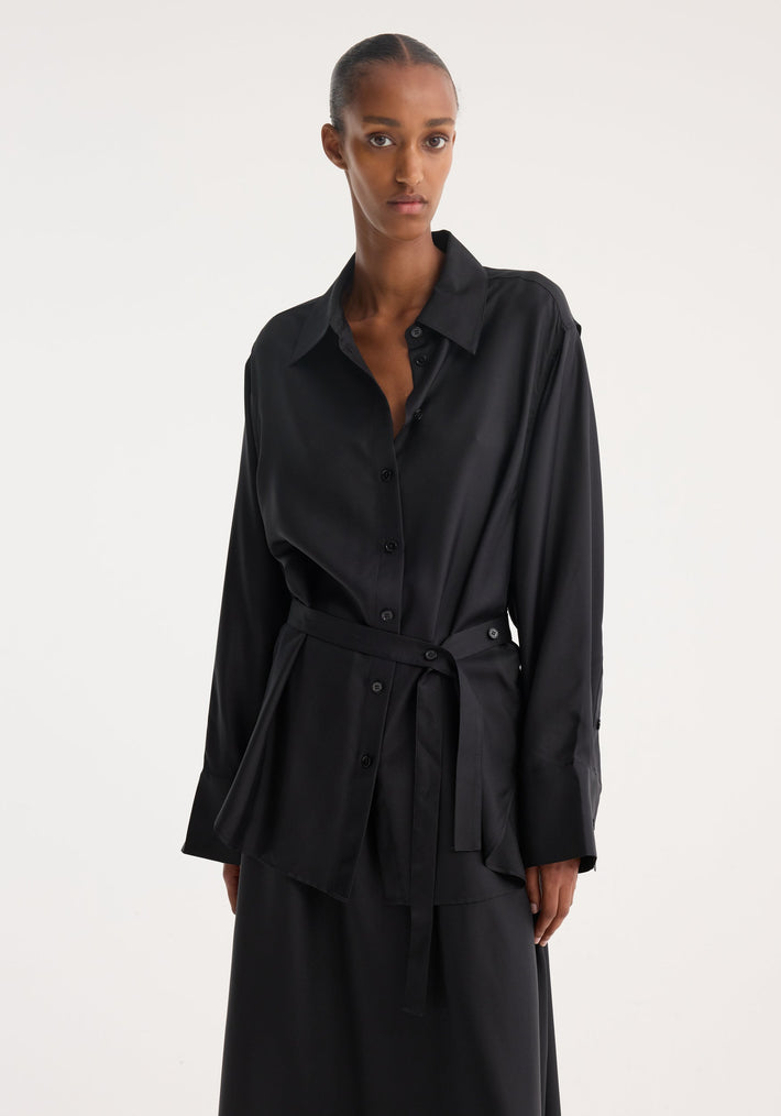 Silk gilet-dress in black, featuring a buttoned wrap belt and open armholes, worn by a model in a minimalist studio setting.