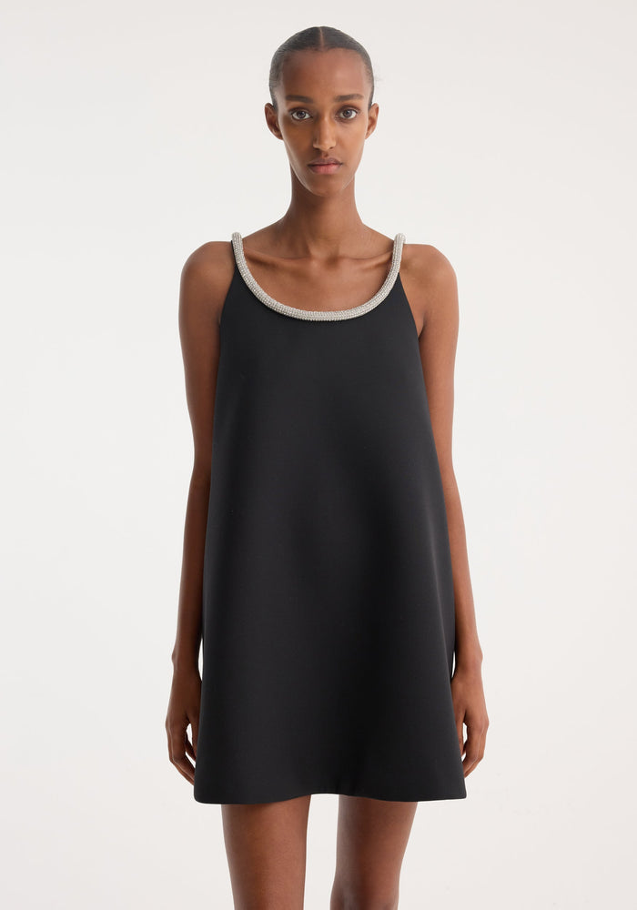 Black sleeveless dress with an applique trim worn by a model on a light gray background