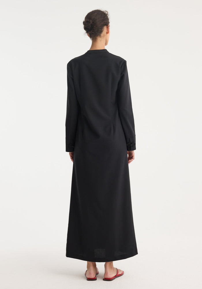 Person in black Mandarin dress with asymmetrical pankou closures, floor-length silhouette, long sleeves, and side split, paired with red slip-on sandals.