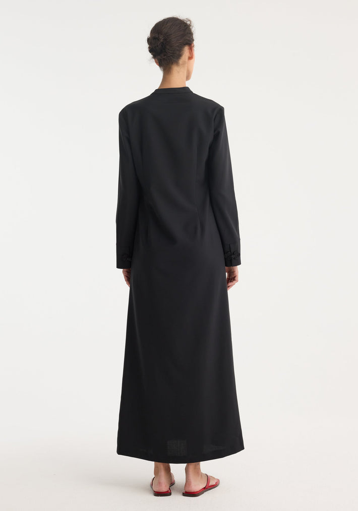 Person in black Mandarin dress with asymmetrical pankou closures, floor-length silhouette, long sleeves, and side split, paired with red slip-on sandals.