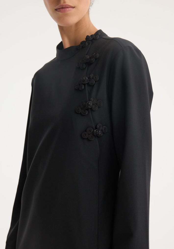 Model wearing Mandarin dress in black, featuring asymmetrical pankou closures on the upper body. Long-sleeved wool-mohair blend with high neckline and intricate detailing.
