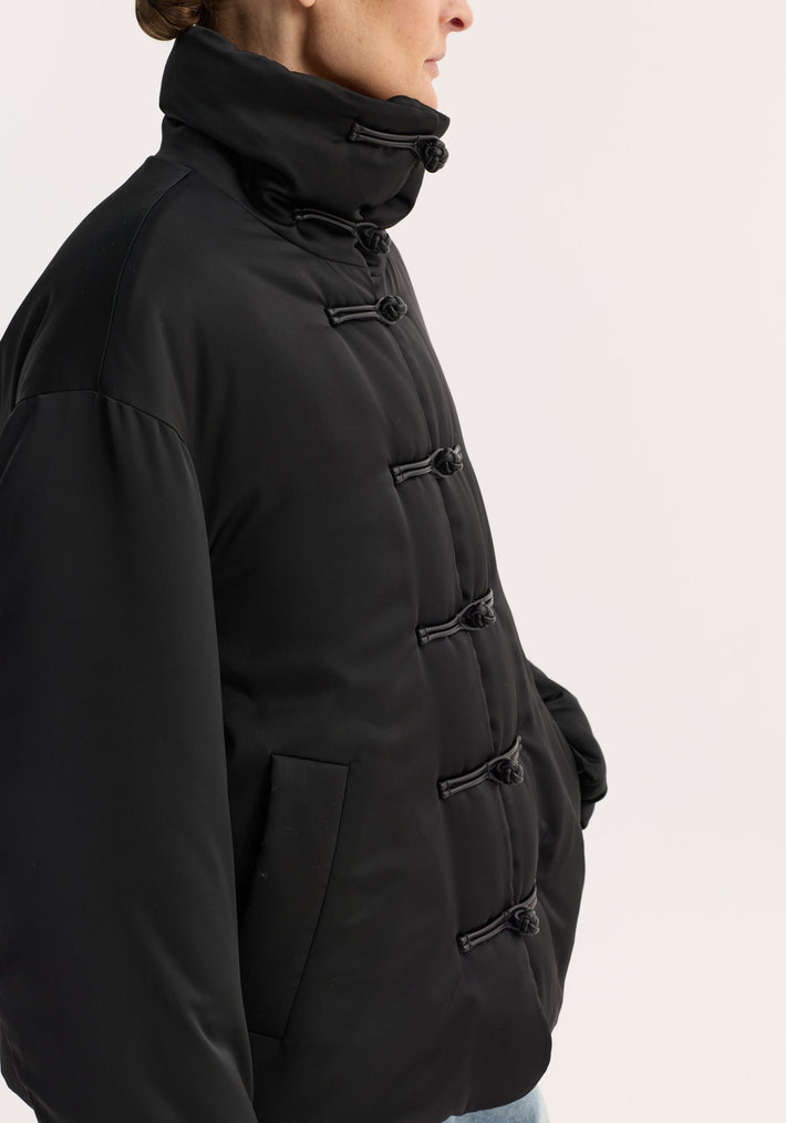 Padded puffer jacket | black with quilted funnel collar, pankou closures, slanted welt pockets, and dropped shoulders, showcased in a close-up side view.