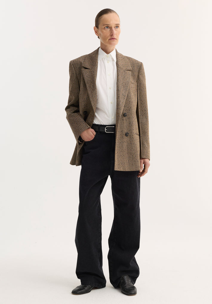 Person wearing a double-breasted blazer with herringbone texture, featuring broad lapels, chest and welt pockets, paired with a white shirt and black trousers.