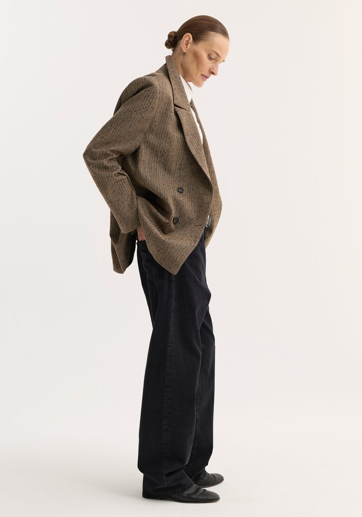 Model in a Double breasted blazer | herringbone, showcasing a refined silhouette with sharp shoulders, chest and welt pockets, paired with loose black trousers.