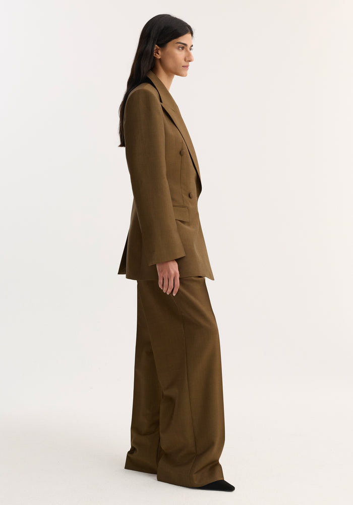 Woman in profile wears Hourglass blazer | golden brown, tailored with sharp notch lapel and cinched waist, paired with matching wide-leg trousers and pointed-toe shoes.