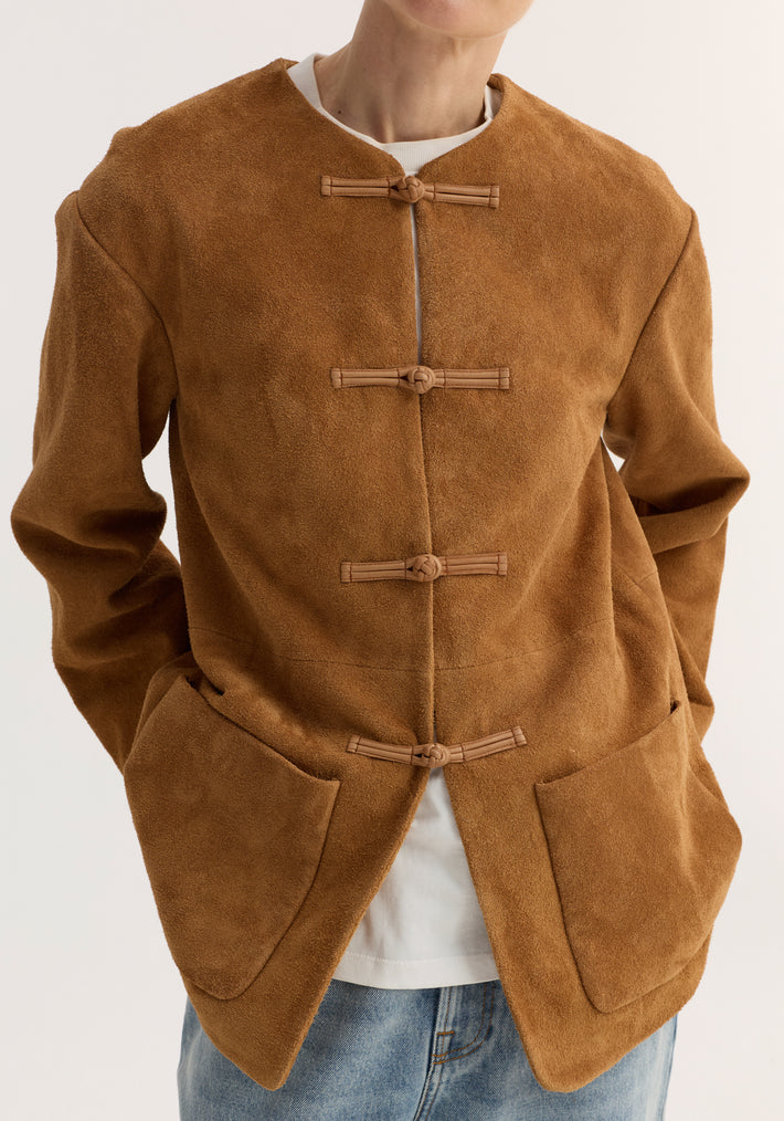 Pankou closure suede jacket in cognac, featuring frog toggle closures, embroidered edges, and patch pockets, worn over a white T-shirt and light-washed jeans.