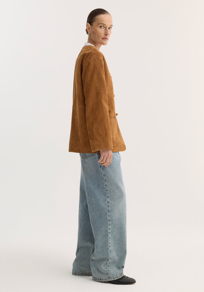 Pankou closure suede jacket in cognac, featuring a side-profile view with embroidered edges, patch pockets, worn over a white top with jeans and slip-on shoes.