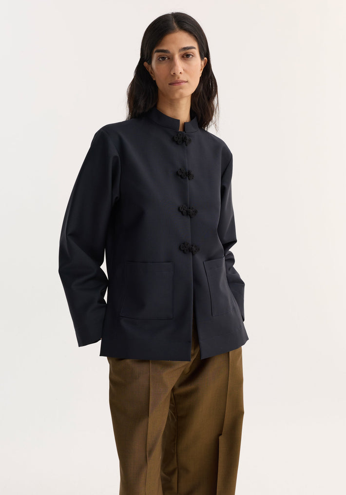 Model wearing Pankou closure jacket in navy with five decorative closures, patch pockets, and straight-leg trousers, showcasing traditional Chinese garment craftsmanship and modern functionality.