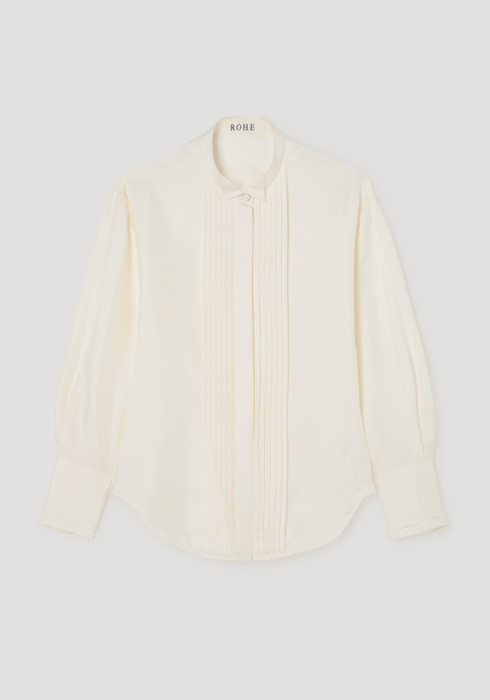 Shaped tuxedo silk shirt | cream featuring a stand-up collar, vertical pintucks, and high cuffs. Crafted from 100% silk, offering a waisted fit and curved hemline.