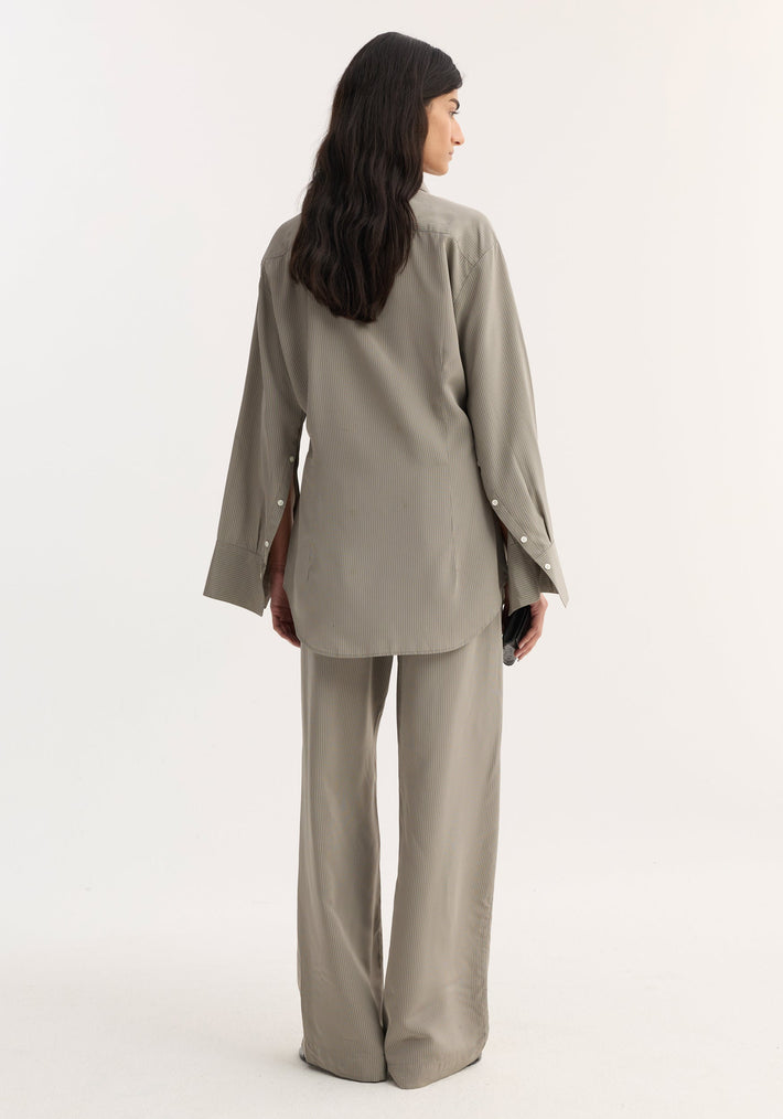 Model in Relaxed shaped shirt | light grey stripe, showing a loose fit, elongated sleeve plackets, and a rounded hem, paired with matching trousers.