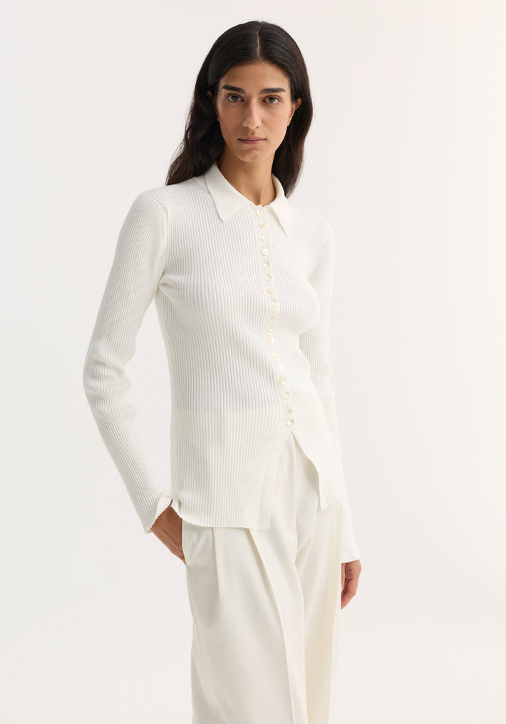Elongated rib cardigan in off white with a pointed collar, button closure, and flared hem, paired with loose, high-waisted trousers.