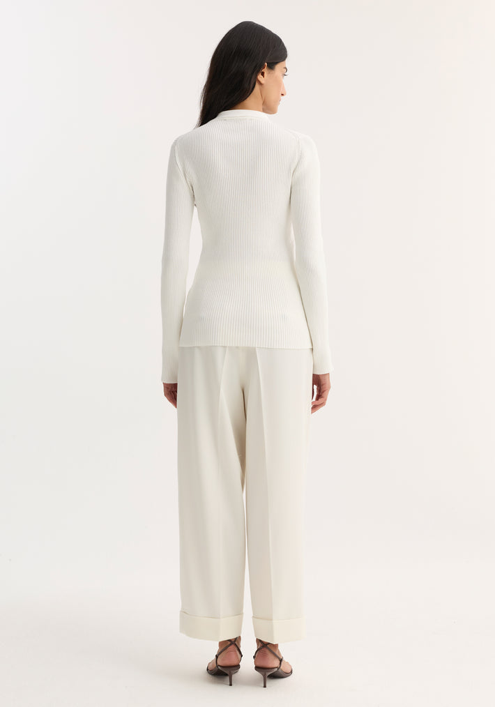 Back view of a woman in an Elongated rib cardigan with button closures and collar, paired with wide-leg trousers and strappy sandals.
