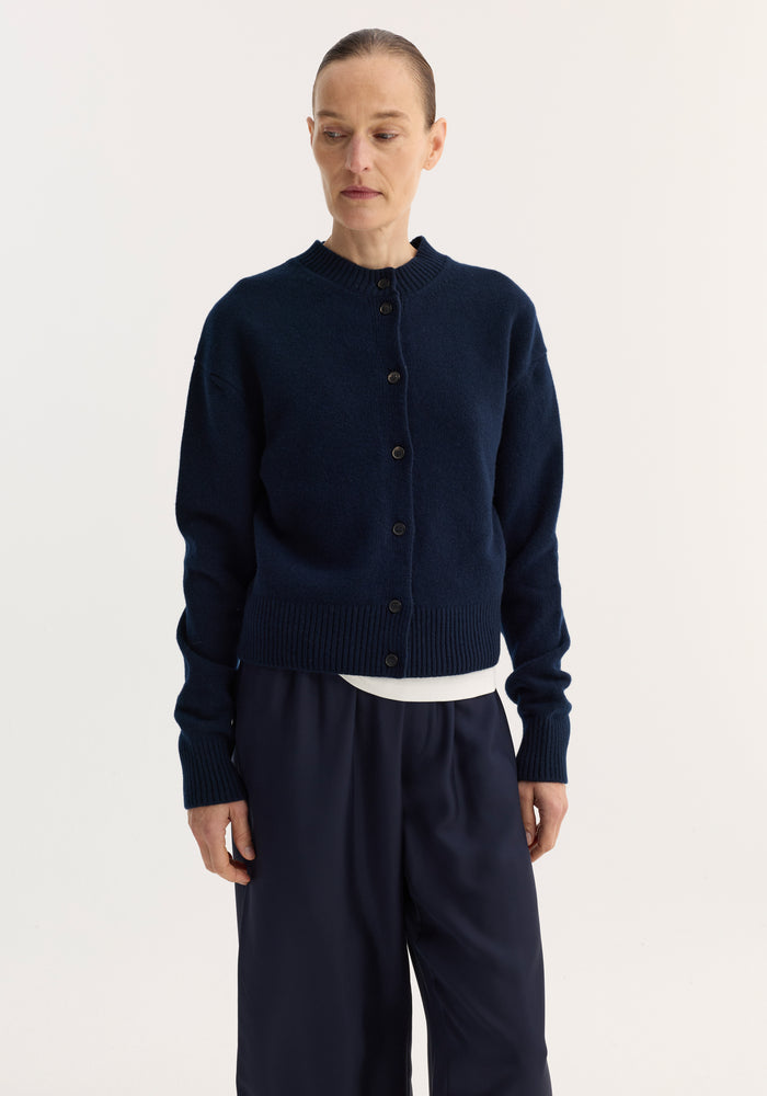 Model wears the Short boiled cardigan | navy, featuring a button-front, ribbed crew neck, drop shoulders, and loose-fit wide-leg trousers against a light backdrop.