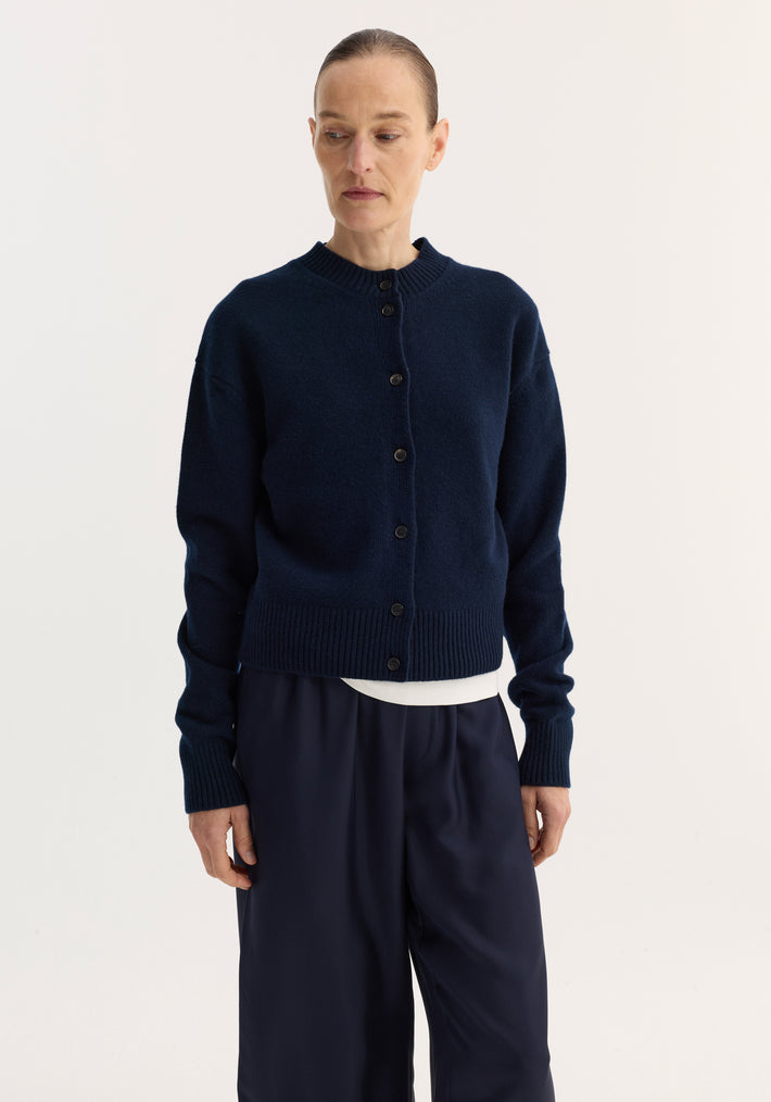Model wears the Short boiled cardigan | navy, featuring a button-front, ribbed crew neck, drop shoulders, and loose-fit wide-leg trousers against a light backdrop.