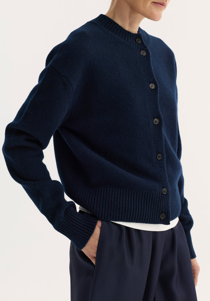 Short boiled cardigan in navy with a high crew neck and drop shoulders, showcasing ribbed cuffs, hem, and a soft, structured felted texture.
