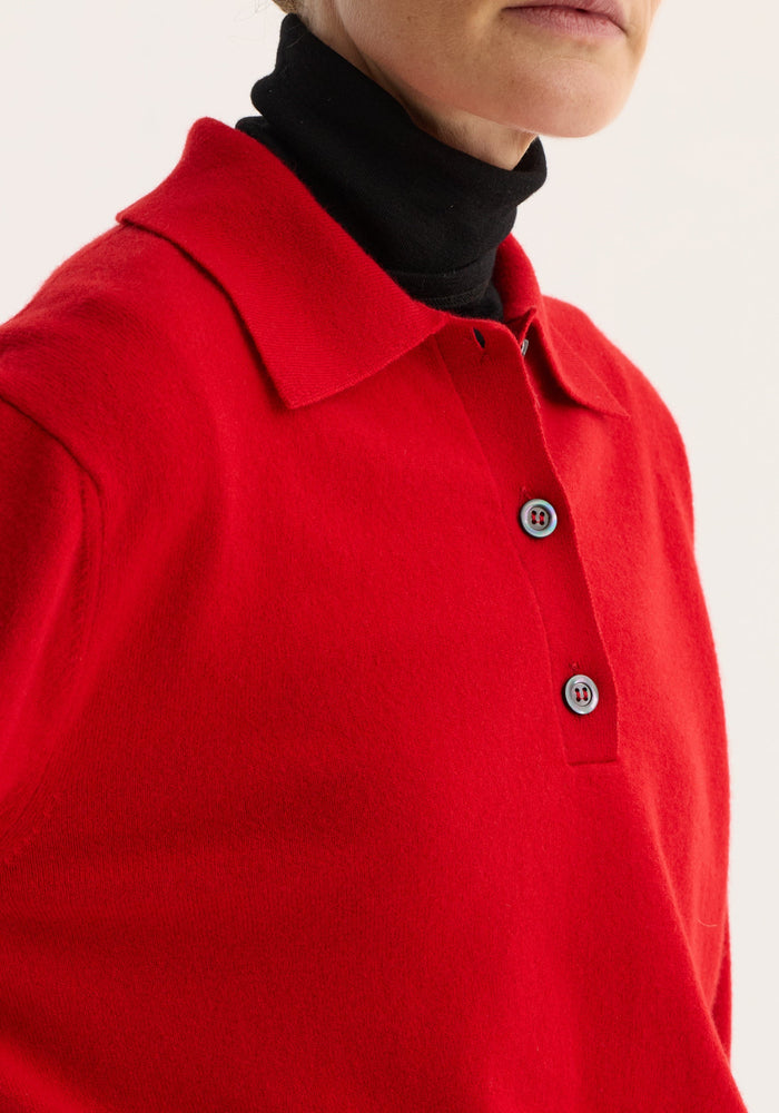 Wool cashmere polo in a vivid red, featuring a relaxed fit, structured collar, and three-button front, layered over a black turtleneck on a model.