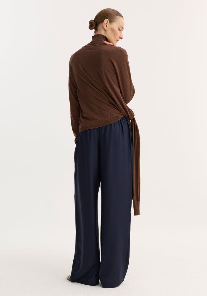 Wide leg silk trousers | night, shown from behind, showcasing their relaxed drape, elasticated waistband, and drawstring, worn by a person with hair in a low bun.