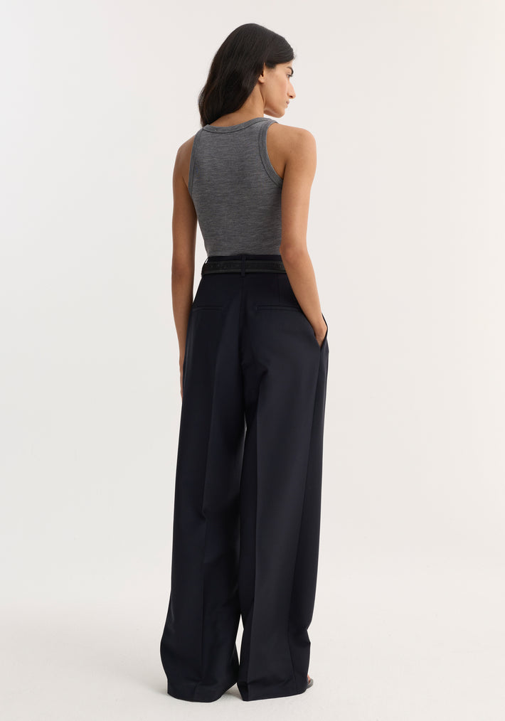 Back view of model wearing mid-waist tailored trousers with wide legs, belted waist, and double pleats, hands in pockets for a relaxed look.