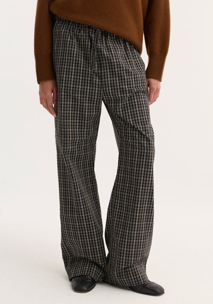 Relaxed fit trousers in black-and-white check with wide legs and drawstring waistband, shown on model with black slip-on shoes and brown sweater.