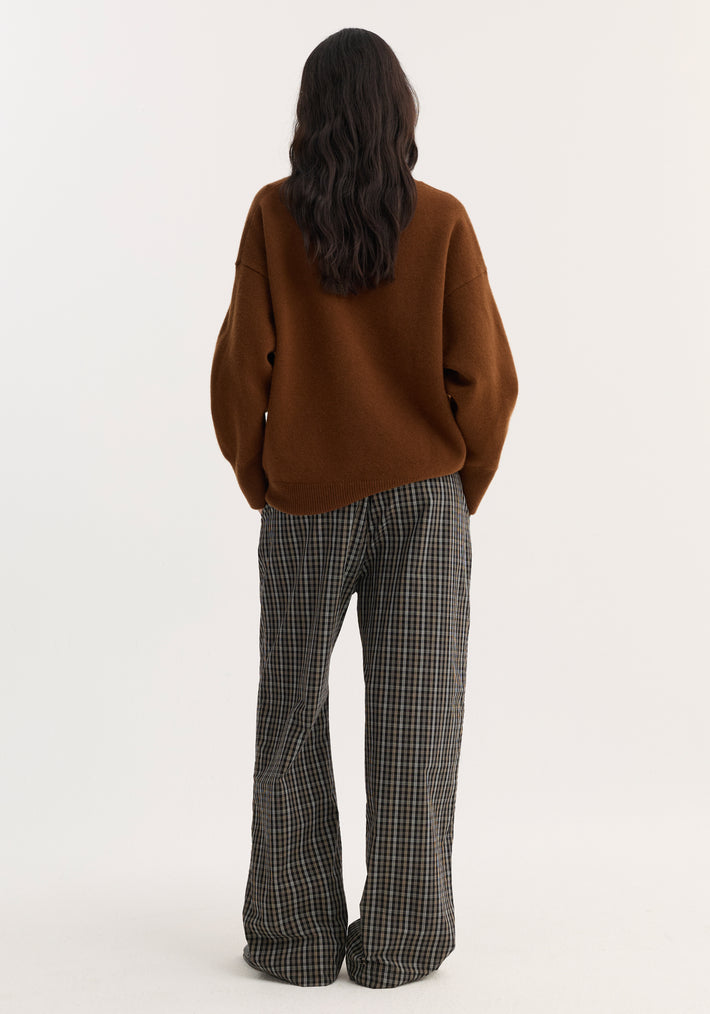 Person wearing Relaxed fit trousers in black/brown check, featuring a wide-leg, high-waisted design with a drawstring waistband, styled with a brown oversized sweater.