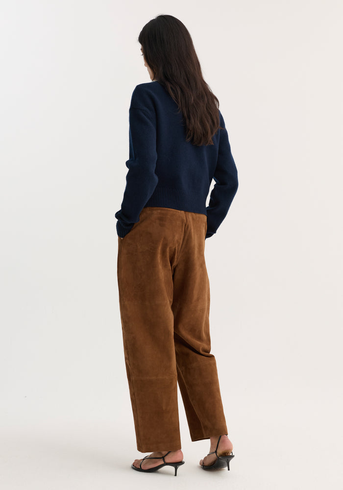 A person wears Sculptural suede trousers | tobacco, showcasing wide barrel legs, panel seam detailing, and back pockets, paired with black slingback sandals.