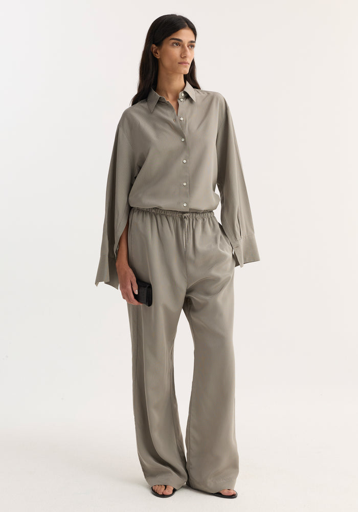 Woman wearing Relaxed fit trousers | light grey stripe, featuring a drawstring waistband and wide leg, styled with a matching shirt and black sandals.