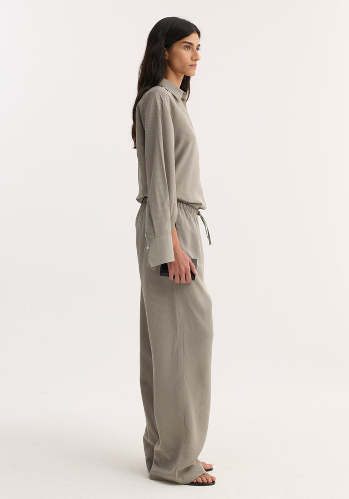 Side-profile of a person wearing Relaxed fit trousers | light grey stripe, featuring a wide leg and drawstring waistband, paired with a matching pinstriped shirt.