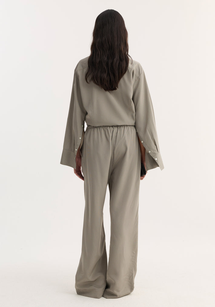 Back view of person in Relaxed fit trousers, light grey stripe, with wide legs and drawstring waistband, paired with a matching pin-stripe shirt, holding a black accessory.
