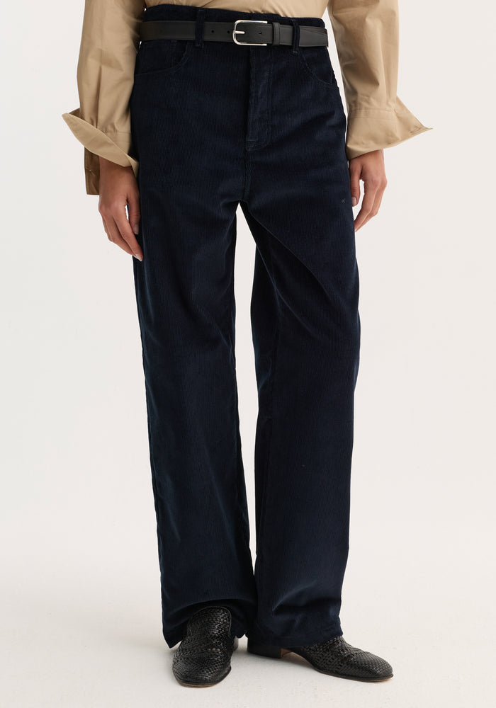 Model wearing Relaxed corduroy trousers | night with a straight-leg fit, black belt, beige shirt, and black woven slip-on shoes.