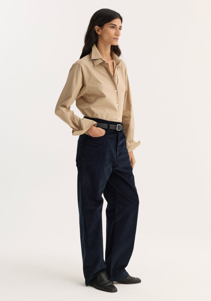 Model wearing Relaxed corduroy trousers | night, navy hue, low-rise, loose leg, denim-style details, paired with a beige shirt and black woven loafers.