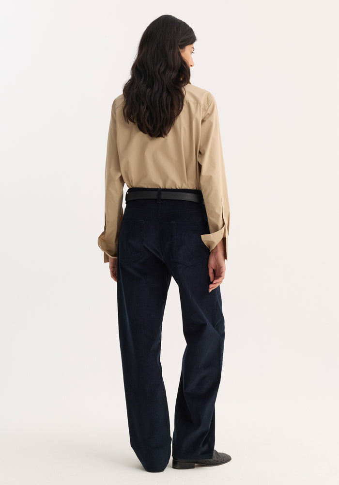 Person wearing Relaxed corduroy trousers | night, featuring wide-leg, low-rise fit, and denim-style details, paired with a light tan shirt and black belt.