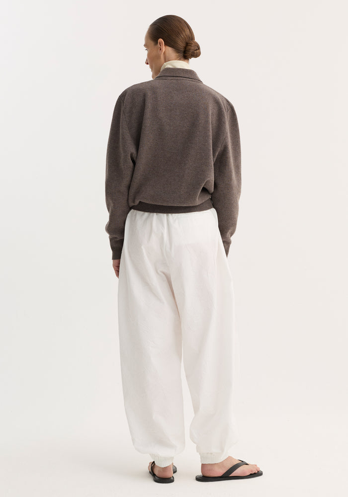 Back view of model in Balloon track pants | optic white, featuring crinkled texture, elastic waistband, voluminous legs, and welt pockets, paired with a muted sweater.