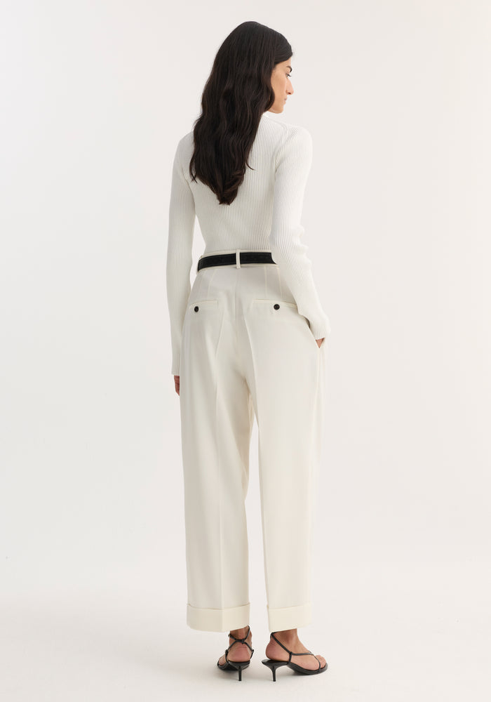 Woman wearing high-waist turn-up trousers with pleats, wide leg, and rolled cuffs, paired with a ribbed top, black belt, and kitten-heel sandals.
