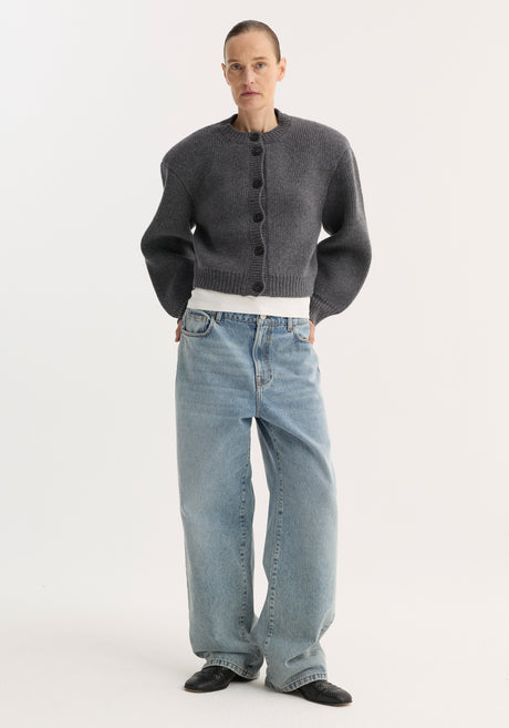 Person in charcoal cardigan and white T-shirt, wearing Signature baggy fit denim, classic blue, with wide-leg, low-waist fit, paired with black slip-on shoes.