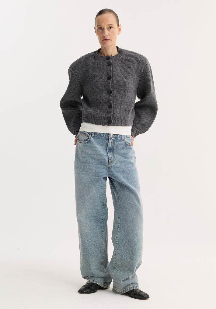 Person in charcoal cardigan and white T-shirt, wearing Signature baggy fit denim, classic blue, with wide-leg, low-waist fit, paired with black slip-on shoes.